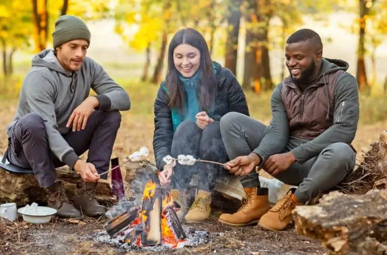 Three people sitting around a campfire in the woods during fall.