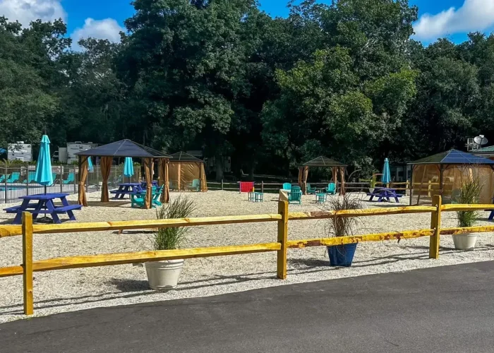 Outdoor seating area with picnic tables and gazebos, enclosed by a yellow wooden fence.